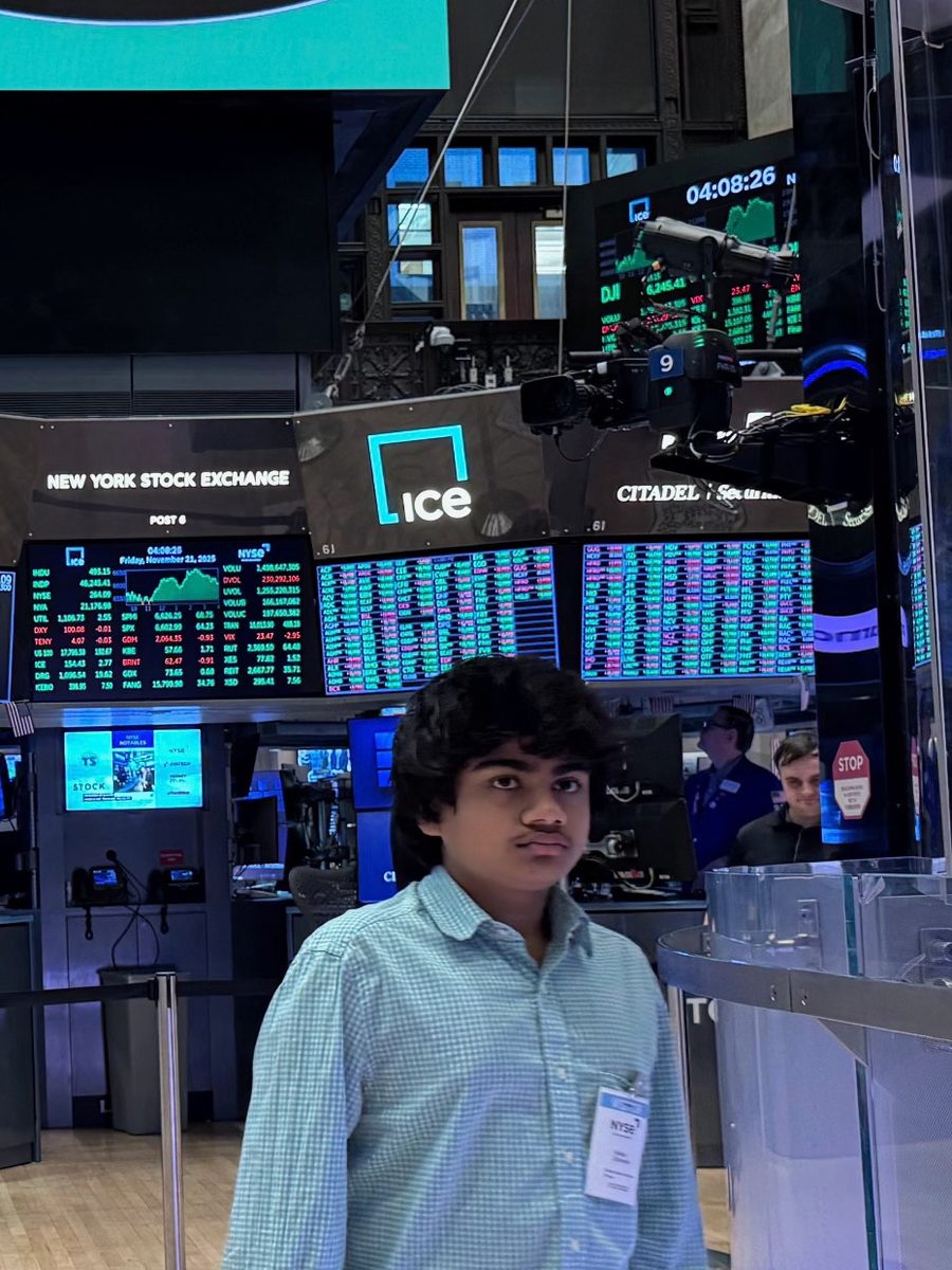 Advay Danwale standing on the trading floor of the New York Stock Exchange, with the price boards behind him.
